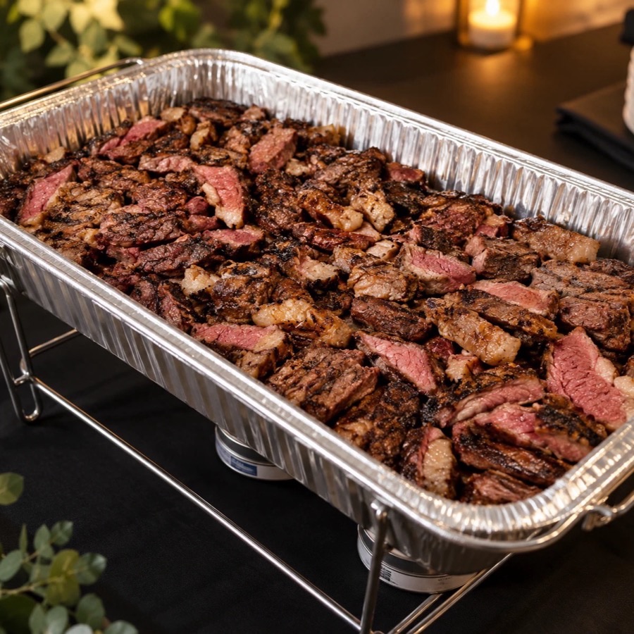 Disposable tray of sliced picanha on a chafing rack, set up buffet style for a drop-off order