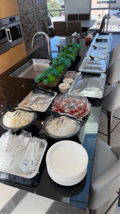 Potato and macaroni salads, croquettes and caprese skewers beside stacked plates and wrapped utensils