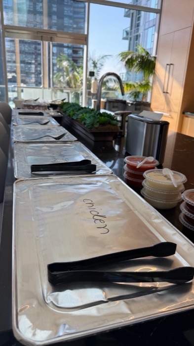 Labelled foil catering trays with serving tongs and portioned sauces on a counter