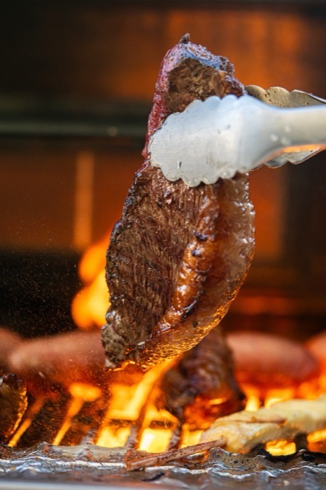Picanha steak held with tongs over an open flame