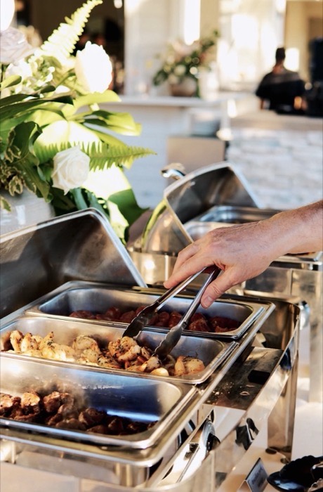 Server plating grilled meat from chafing trays for a guest